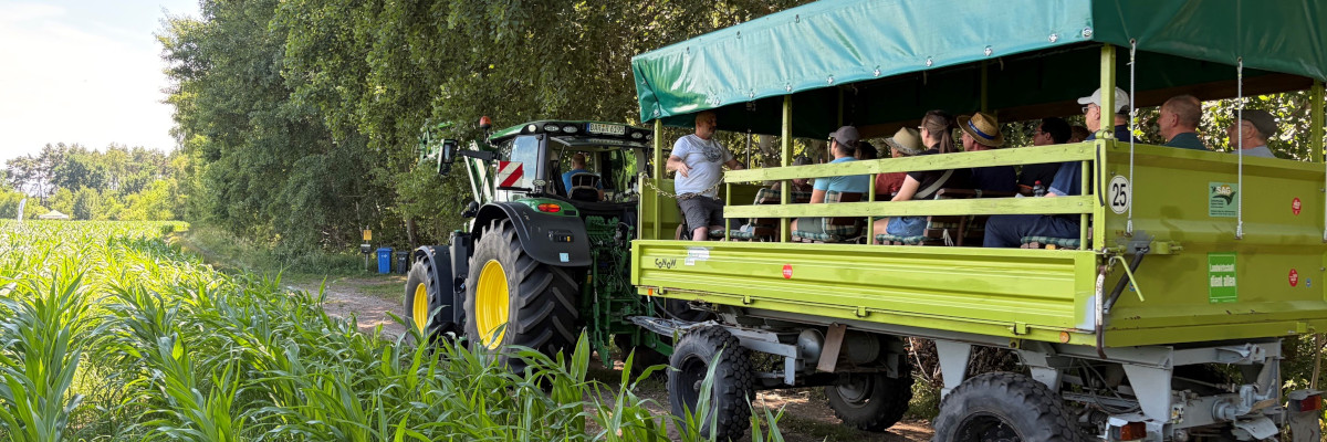 die Teilnehmer der Veranstaltung fahren auf einem Wagen neben dem Feld her