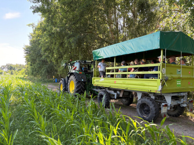 die Teilnehmer der Veranstaltung fahren auf einem Wagen am Feld entlang